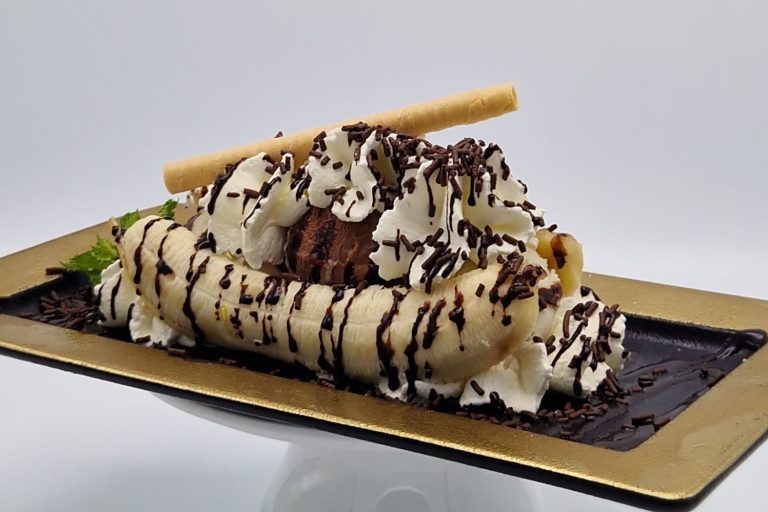 Banane mit Schlagsahne, Schokolade und einem Waffelstäbchen dekoriert.