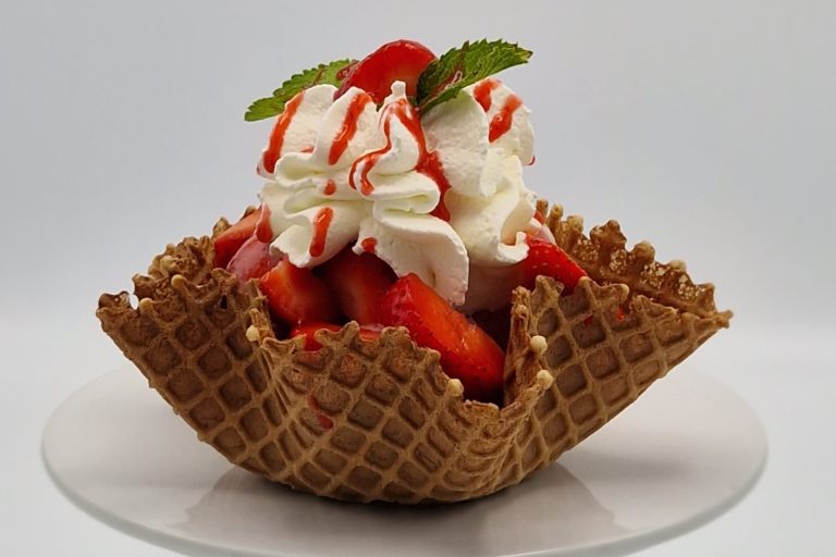 Eiswaffelschale mit Erdbeeren, Schlagsahne und rotem Sirup, garniert mit Minze.