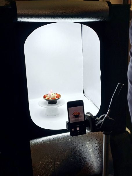 Fotostudio mit beleuchtetem Hintergrund, einem Eisbecher und einem Smartphone.