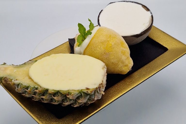 Anrichtung mit Ananas, Zitronen, Kokokusnuss, gefülltem Dessert und einer Schüssel Sahne.