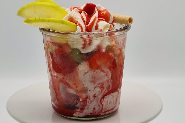 Früchtebecher mit diversen Früchten, Soße, Sahne, Limettenscheiben und einem Keks.