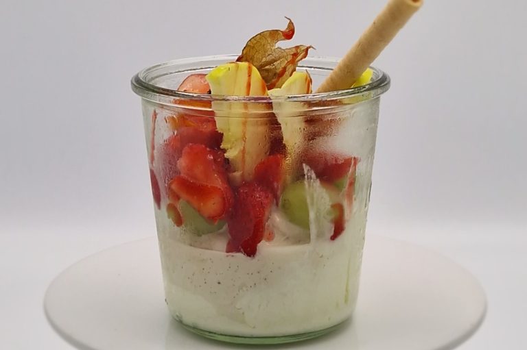 Ein Glas mit Joghurt, frischen Erdbeeren, Vanilleeis und einem Waffelstäbchen.