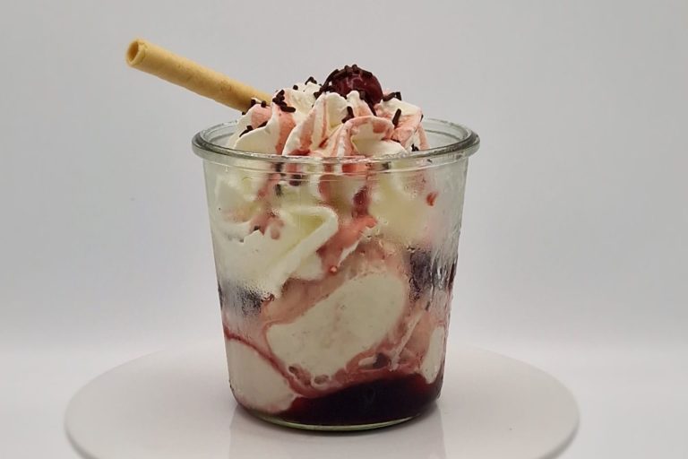 Ein Becher mit Eis, Sahne, Kirschen und einer Waffelrolle obendrauf.