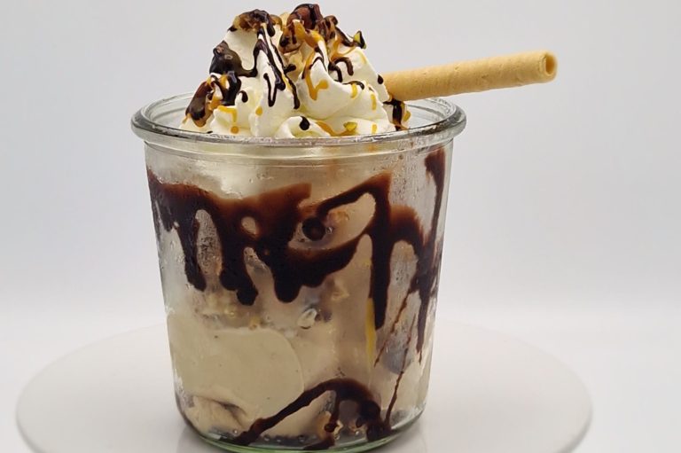Eisbecher mit Sahne, Nüssen, Krokant, Schokoladensauce und einer Waffel.
